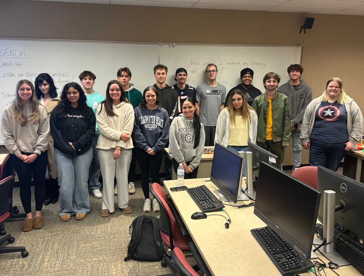 Group of 16 people posing for picture in two rows, all smiling at the camera. People are between the ages of 17 and 26 and are dressed casually.